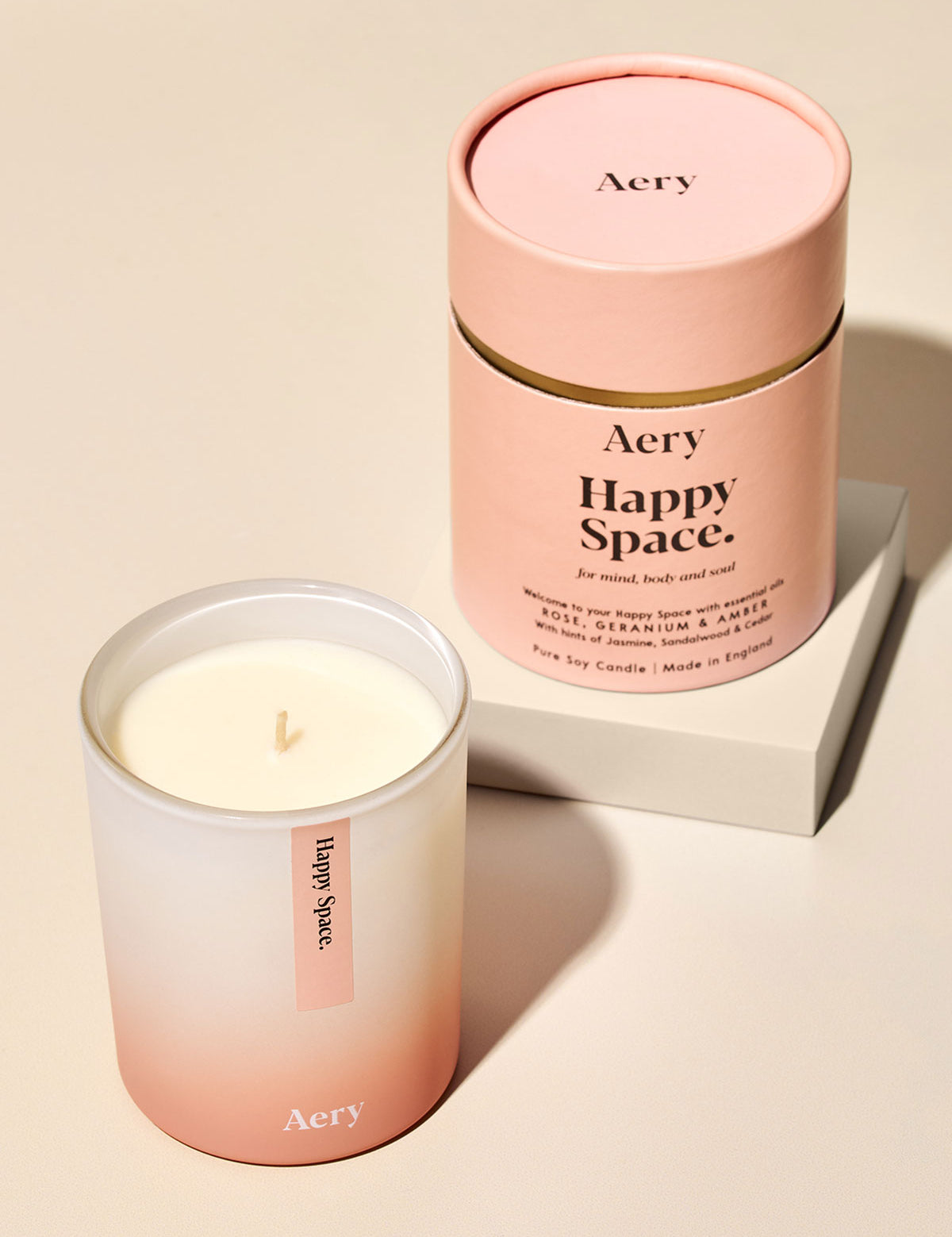 Aery Happy Space Duftkerze aus Sojawachs mit Rosenduft, Geranium und Amber, in rosa-beiger Verpackung und Glas;