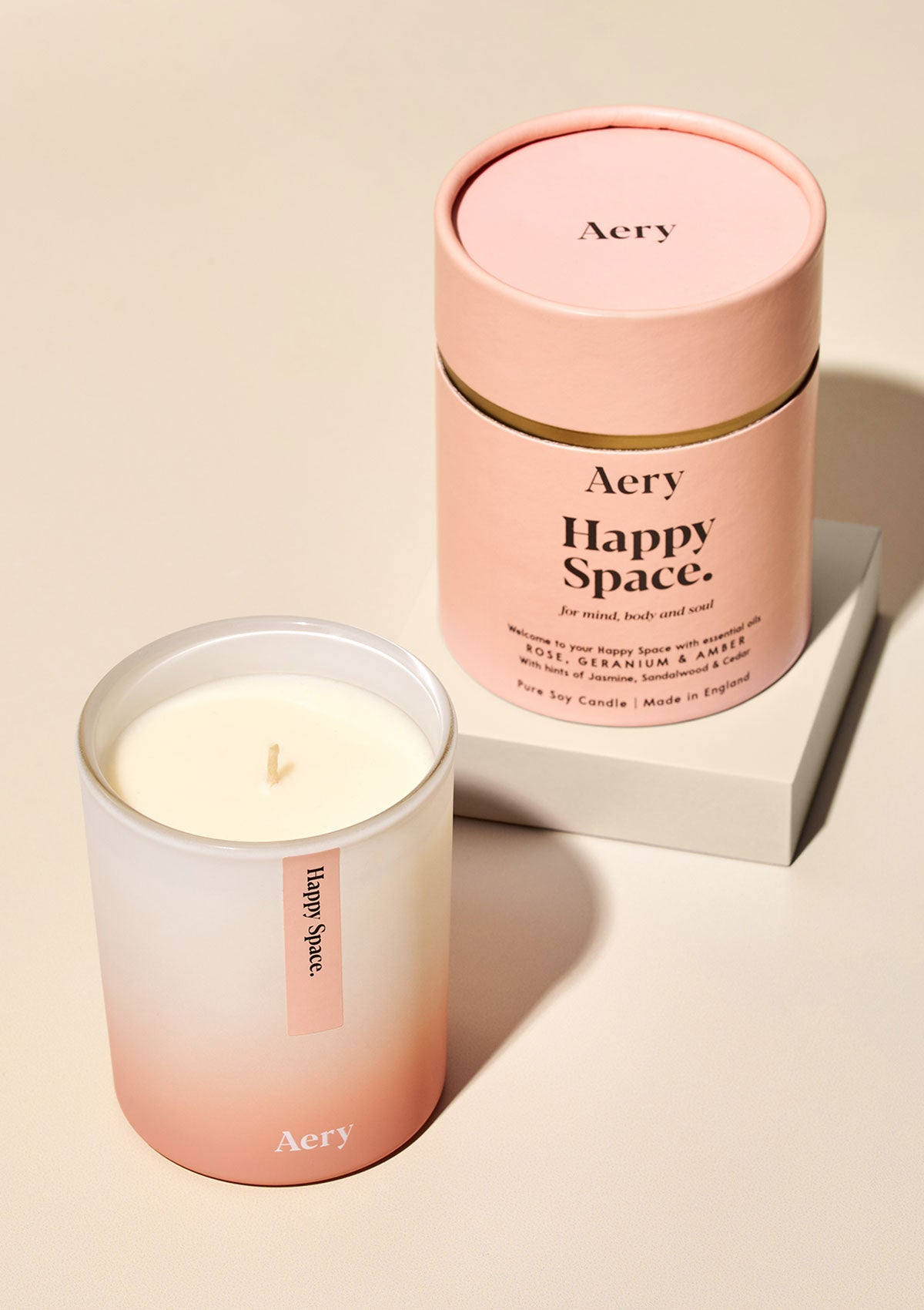 Aery Happy Space Duftkerze aus Sojawachs mit Rosenduft, Geranium und Amber, in rosa-beiger Verpackung und Glas;