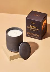 Aery Duftkerze 'Indian Sandalwood' in dunklem Keramikgefäß mit passendem Deckel und Verpackung mit Baumillustration;


