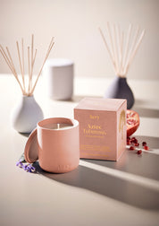Aery Duftkerze 'Aztec Tuberose' in rosa Keramikbehälter mit passendem Deckel und Verpackung, daneben Granatapfelkerne und Duftstäbchen;
