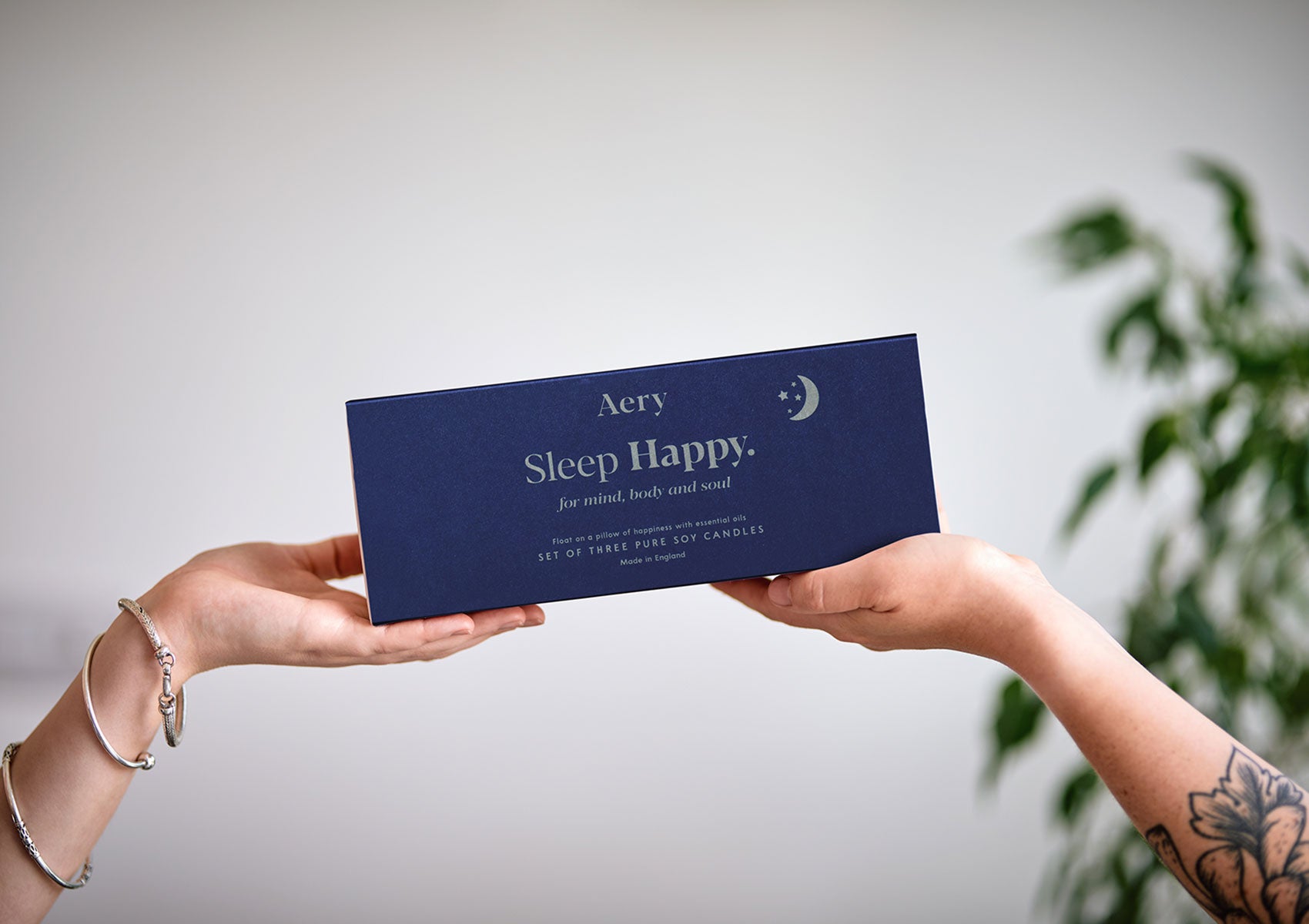 Zwei Hände halten rechts und links die blaue Geschenkbox von Aery "Sleep Happy" mit drei Aromatherapie-Kerzen;