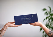 Zwei Hände halten rechts und links die blaue Geschenkbox von Aery "Sleep Happy" mit drei Aromatherapie-Kerzen;