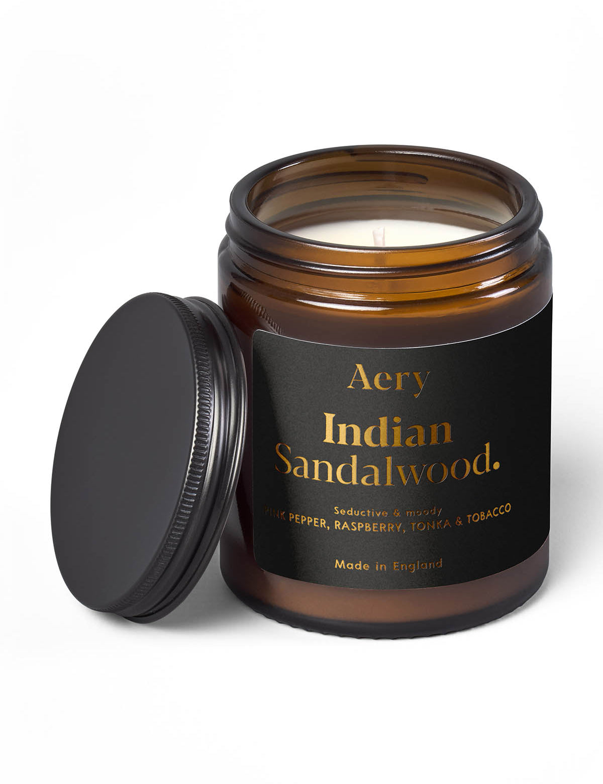 Braune Duftkerze im Glas mit schwarzem Deckel daneben, Marke Aery, Duft 'Indian Sandalwood' mit Noten von Pfeffer, Himbeere, Tonka und Tabak;