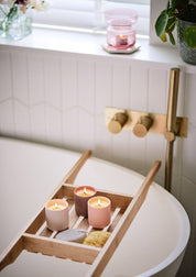 Badewanne mit Holzablage, darauf drei brennende Kerzen, Schwamm und Badeschwamm, goldfarbener Wasserhahn an weiß gefliester Wand;